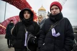 FILE - Women stay in a line to hold a banner during an action against domestic violence on the Patriarshy Bridge, with the Cathedral of Christ the Savior in the background, in Moscow, Russia, Dec. 14, 2019.