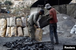 FILE - Palestinian workers fill coal in bags to be sold at charcoal making site, in West Bank village of Yabed, June 11, 2014.