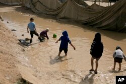 FILE - Children play in a mud puddle in the section for foreign families at al-Hol camp in Hassakeh province, Syria, March 31, 2019.