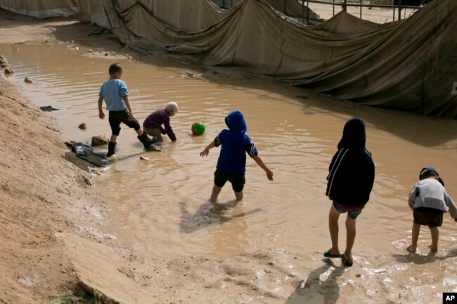 FILE - Children play in a mud puddle in the section for foreign families at al-Hol camp in Hassakeh province, Syria, March 31, 2019.