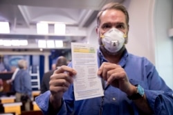 FILE - Journalist Brian Fuss holds up COVID-19 testing information after receiving a coronavirus test by the White House Medical Unit before a news conference with President Trump in the press briefing room at the White House, Apr. 9, 2020.