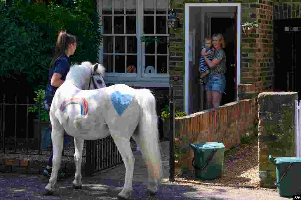 Bryony Blant holding her daughter Alice, who celebrates her 2nd birthday, look at Welsh mountain pony Annie's Wizz held by handler Daisy Cinque outside their home in Twickenham, south west London. 