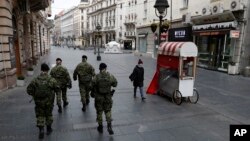 In this March 26, 2020, photo, Serbian army soldiers patrol in Belgrade's main pedestrian street, in Serbia. Since declaring nationwide state of emergency Serbian President Aleksandar Vucic has suspended parliament, giving him widespread powers. (AP Photo/Darko Vojinovic)