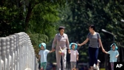 In this June 1, 2017 photo, women walk with children wearing matching hats as they cross a bridge at a public park on International Children's Day in Beijing.