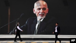 Men walk past a mural of President Ashraf Ghani at Hamid Karzai International Airport, in Kabul, Afghanistan, Aug. 14, 2021.