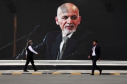 Men walk past a mural of President Ashraf Ghani at Hamid Karzai International Airport, in Kabul, Afghanistan, Aug. 14, 2021.