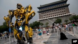 A child stands on a barricade fence looks at a replica model of Transformers character Bumblebee on display in front of Qianmen Gate, as part of a promotion of the movie "Transformers: Age of Extinction" in Beijing, China, June 21, 2014.