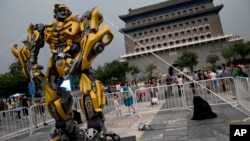 A child stands on a barricade fence looks at a replica model of Transformers character Bumblebee on display in front of Qianmen Gate, as part of a promotion of the movie "Transformers: Age of Extinction" in Beijing, China, June 21, 2014.