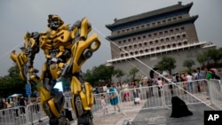 A child stands on a barricade fence looks at a replica model of Transformers character Bumblebee on display in front of Qianmen Gate, as part of a promotion of the movie "Transformers: Age of Extinction" in Beijing, China, June 21, 2014.