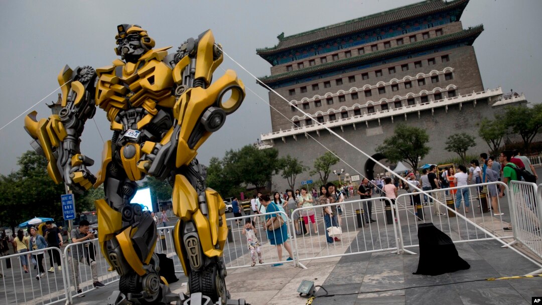 A child stands on a barricade fence looks at a replica model of Transformers character Bumblebee on display in front of Qianmen Gate, as part of a promotion of the movie "Transformers: Age of Extinction" in Beijing, China, June 21, 2014.