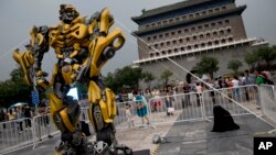 A child stands on a barricade fence looks at a replica model of Transformers character Bumblebee on display in front of Qianmen Gate, as part of a promotion of the movie "Transformers: Age of Extinction" in Beijing, China, June 21, 2014.