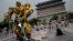 A child stands on a barricade fence looks at a replica model of Transformers character Bumblebee on display in front of Qianmen Gate, as part of a promotion of the movie "Transformers: Age of Extinction" in Beijing, China, June 21, 2014.