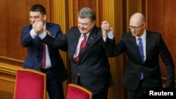 FILE - Ukraine's President Petro Poroshenko, center, holds up the hands of newly appointed Prime Minister Arseny Yatseniuk, right, and newly appointed Parliament Speaker Volodymyr Groysman during a parliament session in Kyiv, Nov. 27, 2014. 