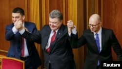 Ukraine's President Petro Poroshenko, center, holds up the hands of newly appointed Prime Minister Arseny Yatsenyuk, right, and newly appointed Parliament Speaker Volodymyr Groysman during a parliament session in Kyiv, Nov. 27, 2014. 