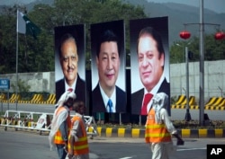 FILE - Municipal workers walk past a billboard showing pictures of Chinese President Xi Jinping, center, with Pakistan's President Mamnoon Hussain, left, and then-Prime Minister Nawaz Sharif on display during a two-day visit by the Chinese president, April 20, 2015.