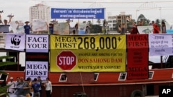 ບັນດານັກເຄື່ອນໄຫວ ຊາວກຳປູເຈຍ ຂອງອົງການ ທີ່ບໍ່ຂຶ້ນກັບລັດຖະບານ (NGOs) ຢູ່ໃນເຮືອນຳທ່ຽວ ທີ່ Tonle Sap ໃນນະຄອນຫຼວງພະນົມເປັນ ຮ້ອງໂຮຄຳຂວັນ ໃນລະຫວ່າງ ການປະທ້ວງ ຕໍ່ຕ້ານໂຄງການເຂື່ອນ ດອນສະໂຮງ, ເມື່ອວັນພະຫັດ ທີ 11 ກັນຍາ 2014. ພວກນັກເຄື່ອນໄຫວນັ້ນ ໃຊ້ເຮືອນຳທ່ຽວ ເພື່ອໂຄສະນາ ການຄັດຄ້ານ ຕໍ່ການສ້າງເຂື່ອນໄຟຟ້າ ອັນໃຫຍ່ໂຕນັ້ນ. (AP Photo/Heng Sinith) 