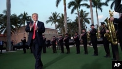 U.S. President Donald Trump listens to the Palm Beach Central High School Band as they play at his arrival at Trump International Golf Club in West Palm Beach, Fla., where he will golf Friday with Japanese Prime Minister Shinzo Abe.