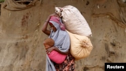A displaced Somali woman carries a child and her belongings as she arrives at a temporary dwelling after fleeing famine in the Marka Lower Shebbele regions to the capital Mogadishu, Sept. 20, 2014. 