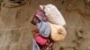 A displaced Somali woman carries a child and her belongings as she arrives at a temporary dwelling after fleeing famine in the Marka Lower Shebbele regions to the capital Mogadishu, Sept. 20, 2014. 