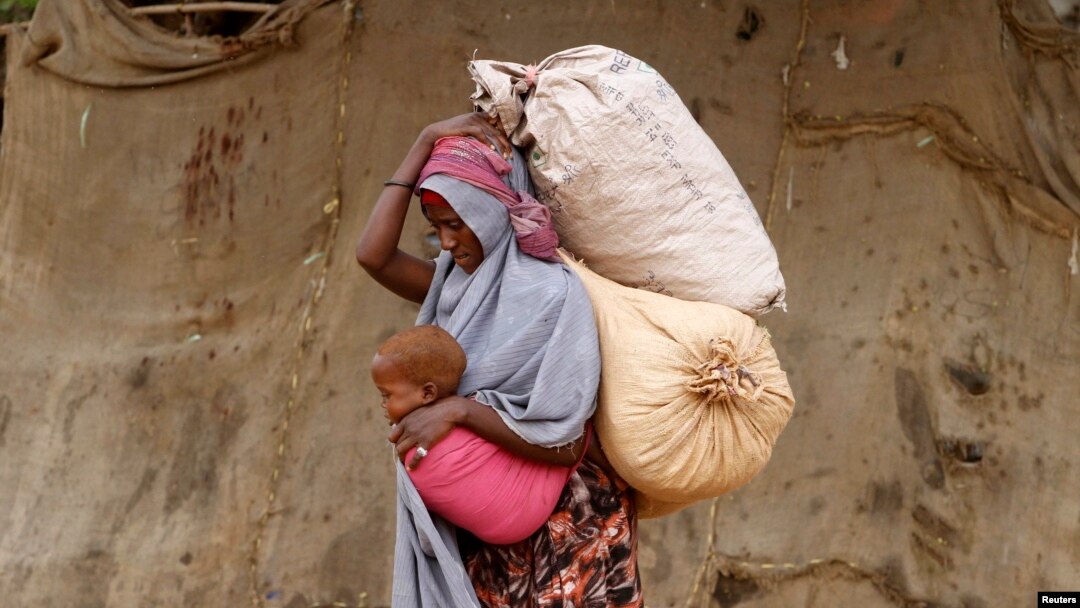 A displaced Somali woman carries a child and her belongings as she arrives at a temporary dwelling after fleeing famine in the Marka Lower Shebbele regions to the capital Mogadishu, Sept. 20, 2014. 