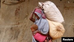 A displaced Somali woman carries a child and her belongings as she arrives at a temporary dwelling after fleeing famine in the Marka Lower Shebbele regions to the capital Mogadishu, Sept. 20, 2014. (REUTERS/Feisal Omar)