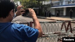 FILE - A journalist and a police officer take pictures of each other as people protest against the military coup in Yangon, Myanmar, February 23, 2021.