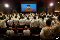 FILE - Hezbollah scouts raise their fists and cheer as they listen to a speech by Hezbollah leader Sayyed Hassan Nasrallah, via a video link, during an annual anniversary rally for Hezbollah al-Mahdi scouts, in southern Beirut, Lebanon, April 22, 2019.