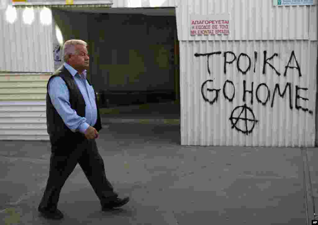 A man walks by graffiti that reads "Troika out" in the old city of capital Nicosia, Cyprus, March 19, 2013.