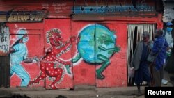 Vendors, carrying traditional medicine in jerrycans, stand outside a stall which has graffiti against the spread of the coronavirus disease (COVID-19) within Kibera slums in Nairobi, Kenya, July 6, 2020. 