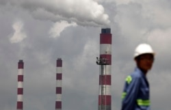 資料照：浙江寧波港的一名工人站在火力發電廠的大煙囪前。