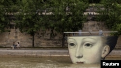 People hang out by the River Seine near an art installation for the Olympics, in Paris, France, August 3, 2024. 