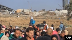 FILE—Palestinians fleeing the fighting in Gaza walk on a road while monitored by Israeli soldiers (background) guarding Palestinian detainees in a military truck, in the Zeitoun district of the southern part of the Gaza Strip on November 19, 2023.