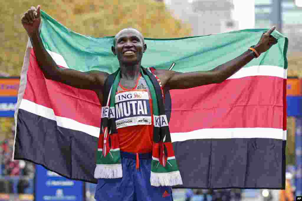 Geoffrey Mutai dari Kenya memegang bendera Kenya setelah memenangkan maraton kategori pria. (AP/Kathy Willens)