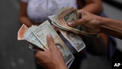 Un trabajador del transporte público de Caracas cuenta bolívares y dólares mientras busca cambio para una pasajero, el 9 de agosto de 2023. Venezuela vive una crisis económica interna mientras su deuda externa es considerada muy elevada.