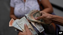 Un trabajador de un autobús público cuenta bolívares venezolanos y dólares estadounidenses, mientras da cambio para un pasajero, en el barrio Quinta Crespo de Caracas, Venezuela, el miércoles 9 de agosto de 2023