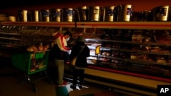 FILE - Customers use a cellphone light to shop in grocery store in Dallas, Feb. 16, 2021. 