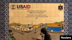 ARCHIVO - Un palestino camina junto a un cartel de cerámica de un proyecto de la Agencia de Estados Unidos para el Desarrollo Internacional (USAID) en Hebrón, en Cisjordania ocupada por Israel, el 31 de enero de 2019. 