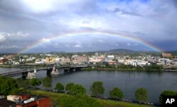 FILE - In this May 11, 2017, photo, a rainbow pops out under dark rain clouds over the Willamette River in downtown Portland, Oregon.