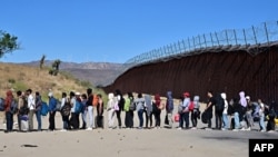 Migrantes esperan en fila con la esperanza de ser procesados ​​por los agentes de Aduanas y Patrulla Fronteriza después de llegar a Jacumba Hot Springs, California, luego de caminar bajo un intenso calor desde México a Estados Unidos, 5 de junio de 2024. 