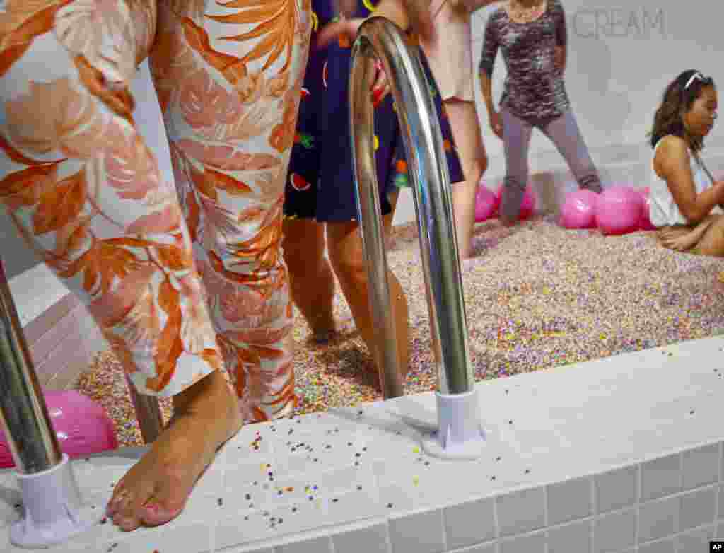 Visitors walk into a large pool filled with faux confetti-colored sprinkles, the biggest attraction of ice cream-themed works of art previewed at the Museum of Ice Cream, July 28, 2016, in New York. The museum opens on Friday and runs through Aug. 31.