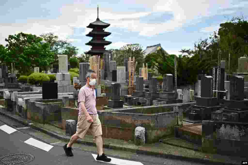 A man wearing a face mask walks in a cemetery near the Honmonji Goju-no-to Pagoda in Tokyo, Japan.