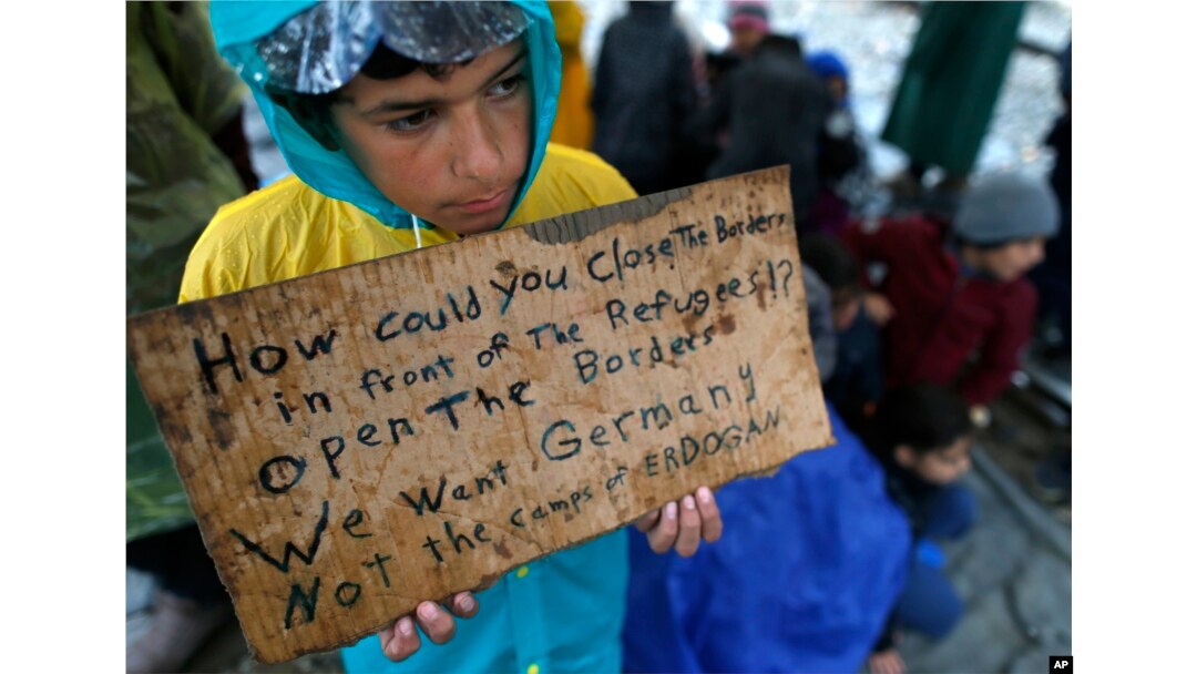 FILE - A migrant boy shows a banner saying he wants to travel to Germany rather than camps set up by Turkey, during a protest demanding the opening of the border between Greece and Macedonia in the northern Greek border station of Idomeni, Greece, March 23, 2016.