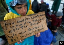 FILE - A migrant boy shows a banner saying he wants to travel to Germany rather than camps set up by Turkey, during a protest demanding the opening of the border between Greece and Macedonia in the northern Greek border station of Idomeni, Greece, March 23, 2016.