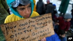 FILE - A migrant boy shows a banner saying he wants to travel to Germany rather than camps set up by Turkey, during a protest demanding the opening of the border between Greece and Macedonia in the northern Greek border station of Idomeni, Greece, March 23, 2016. 