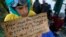 FILE - A migrant boy shows a banner saying he wants to travel to Germany rather than camps set up by Turkey, during a protest demanding the opening of the border between Greece and Macedonia in the northern Greek border station of Idomeni, Greece, March 23, 2016. 