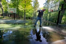 In this Thursday, June 4, 2020 photo, trip leader Gordon Anderson power washes an outdoor basketball court at the Camp Winnebago summer camp in Fayette, Maine. The boys camp is going ahead with plans to open with a reduction in the number of campers.