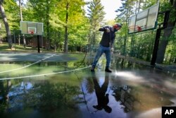 In this Thursday, June 4, 2020 photo, trip leader Gordon Anderson power washes an outdoor basketball court at the Camp Winnebago summer camp in Fayette, Maine. The boys camp is going ahead with plans to open with a reduction in the number of campers.