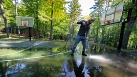 In this Thursday, June 4, 2020 photo, trip leader Gordon Anderson power washes an outdoor basketball court at the Camp Winnebago summer camp in Fayette, Maine. The boys camp is going ahead with plans to open with a reduction in the number of campers.