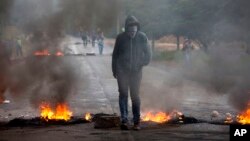 An anti-government protester stands at a burning barricade erected by protesters to block the road to Valle de los Angeles, on the outskirts of Tegucigalpa, Honduras, Dec. 7, 2017. 