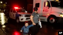 Una mujer con un niño que forma parte de una caravana de migrantes que buscan llegar a Estados Unidos camina frente a un auto policial desde la central de autobuses de San Pedro Sula, Honduras, la noche del lunes.